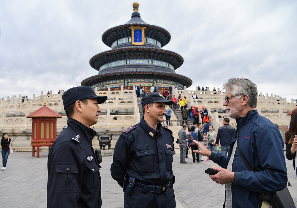 4月25日，在北京天坛祈年殿前，参与中意警务联合巡逻的中方警员丁振（左）、意方警员法比奥·福尔图纳（中）与一名澳大利亚游客交流。