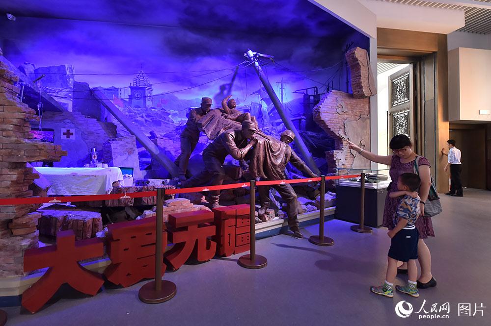 7月24日，在“铭记光辉历史　开创强军伟业——庆祝中国人民解放军建军90周年主题展览”上，一位母亲正在给儿子讲述“汶川地震”时的情景。（人民网记者 翁奇羽 摄）