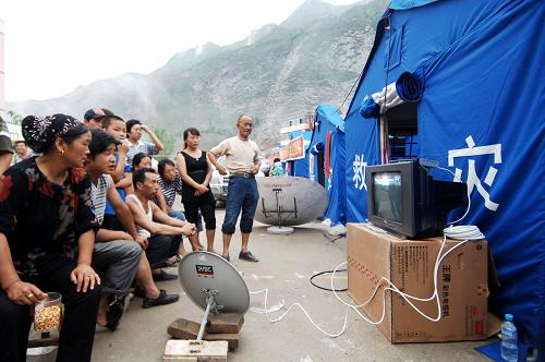 На фото: 12 августа, в третьей средней школе уезда Чжоуцюй пострадавшие смотрят телевизор во временных пунктах жилья.