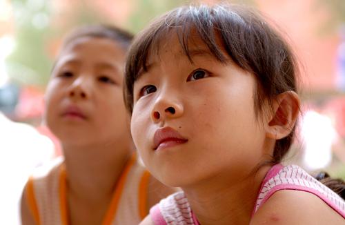 На фото: 16 августа 2010 года, в одном временном пункте жилья в первой средней школе уезда Чжоуцюй 9-летняя Хуан Жун и ее 6-летний брат Хуан Лицян смотрят телевизор на открытом воздухе. 