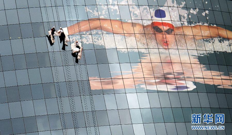 На фото: 9 июля в Лондоне, в штаб-квартире компании «GlaxoSmithKline», которая является одной из 500 крупных компаний в мире и одним из спонсоров Олимпиады-2012; рабочие убирают здание и размещают огромную олимпийскую афишу.