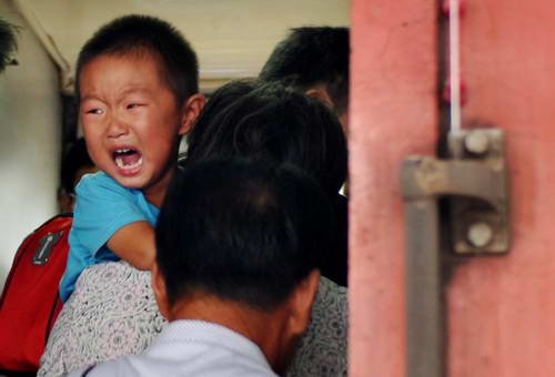 На фото: на вокзале Ханчжоу дедушка несет на руках мальчика из провинции Хэнань, поднимаясь в поезд, мальчик плачет из-за расставания с родителями, которые стоят на платформе.