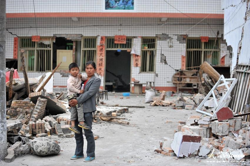 На фото: в деревне Гучэн уезда Лушань, Сяо Цюнь с сыном на руках стоит перед своим домом. До землетрясения Сяо Цюнь готовила дома лапшу, еще вода не успела закипеть, как начались толчки.