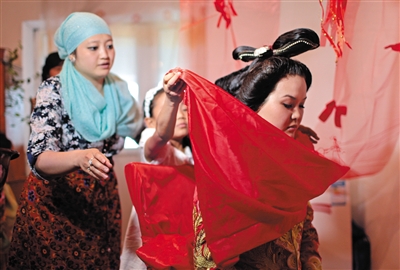 Молодежь из семьи жениха снимают красное покрывало с невесты, подают ей чашу с водой, невеста двумя руками осторожно сбрызгивает лицо.