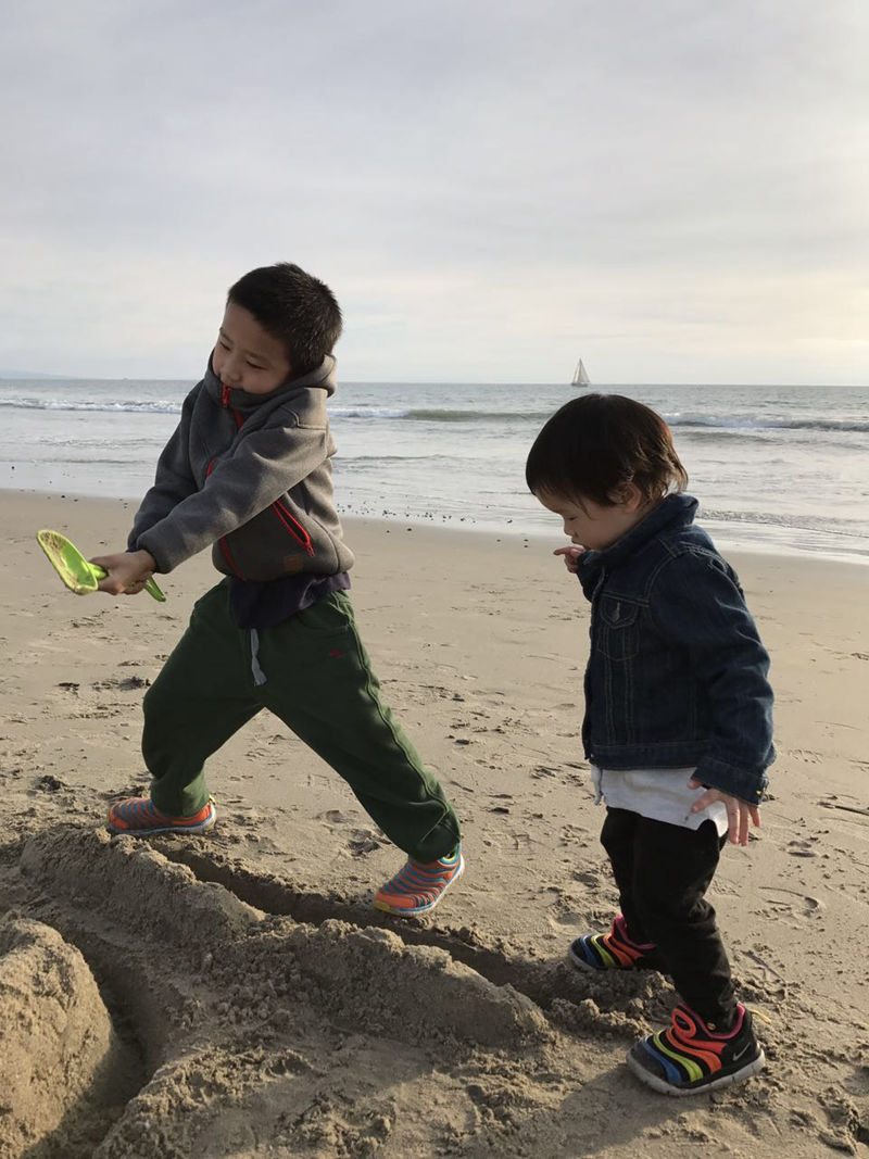 На фото: Лэлэ со старшим братом играет с песком на морском побережье.