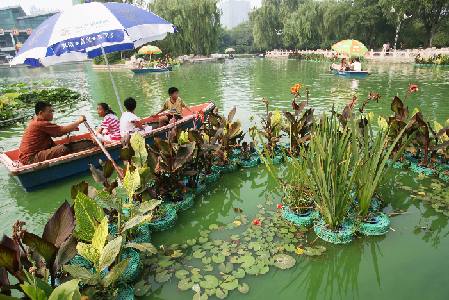 Visitantes paseando en bote por el Jardín Botánico de Jinan, acompañados de macetas colocadas en el lago destinadas a purificar el agua y hermosear el entorno.