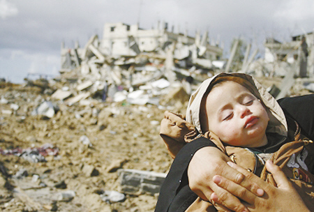 (Foto: Una mujer palestina sostiene a su hijo frente a un edificio destruido)