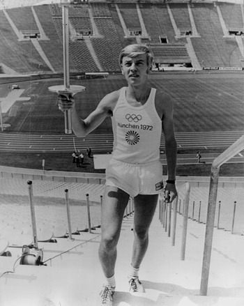 Full-length image of German runner Guenter Zahn holding the Olympic torch while standing on the steps of Munich stadium during a rehearsal for the opening ceremony, Munich, Germany. Zahn served as the relay runner for the last leg of the Olympic torch lighting.