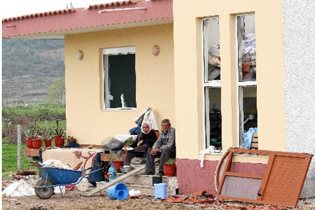 An Albanian couple sit in front of their destroyed house in the village of Gerdec, Albania, Sunday, March 16, 2008. Troops and police cordoned off a smoldering army depot north of the Albanian capital as crews searched Sunday for workers missing following a chain of explosions Saturday that killed at least nine people and injured hundreds.