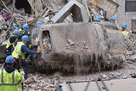 Workers flip over a car to get to a gas shut-off valve after a construction crane collapsed over a residential building in New York March 15, 2008. 