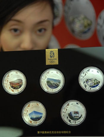 A saleswoman shows a set of commemorative badges featuring five of the venues for the Beijing Olympic Games: (from top left to bottom right ) the National Stadium, or 'Bird's Nest', Qingdao Olympic Sailing Center, Hong Kong Olympic Equestrian Venue, National Aquatics Center, or 'Water Cube', and Shenyang Olympic Stadium , in Beijing, March 16, 2008.