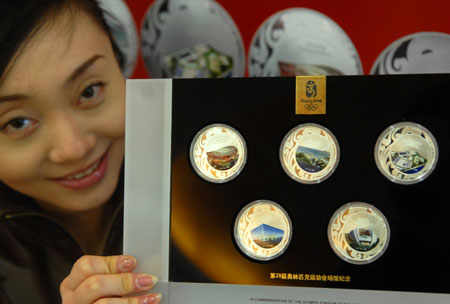 A saleswoman shows a set of commemorative badges featuring five of the venues for the Beijing Olympic Games: (from top left to bottom right ) the National Stadium, or 'Bird's Nest', Qingdao Olympic Sailing Center, Hong Kong Olympic Equestrian Venue, National Aquatics Center, or 'Water Cube', and Shenyang Olympic Stadium , in Beijing, March 16, 2008.