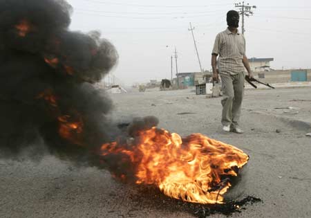 A fighter from the Mahdi Army militia stands guard near a burning tyre on a road in Baghdad's Sadr City March 26, 2008. Fourteen people were killed and more than 140 wounded in clashes between security forces and Shi'ite militants in Baghdad's Sadr City slum, a medical source said on Wednesday. 