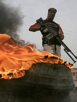 A fighter from the Mahdi Army militia stands guard near a burning tyre on a road in Baghdad's Sadr City March 26, 2008. Fourteen people were killed and more than 140 wounded in clashes between security forces and Shi'ite militants in Baghdad's Sadr City slum, a medical source said on Wednesday.