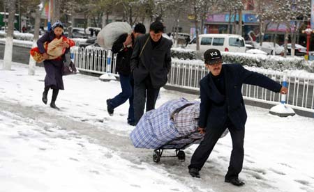 People carrying luggages walk in the snow in Urumqi, capital of northwest China's Xinjiang Uygur Autonomous Region, on April 18, 2008. 