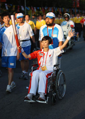 Torchbearer Wang Qihong sitting in a wheelchair holds up the torch during the 2008 Beijing Olympic Games torch relay in Shenzhen, south China's Guangdong Province, on May 8, 2008.