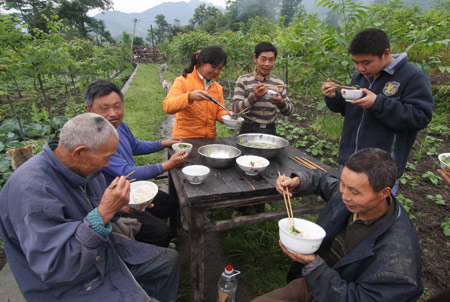 Local residents dine on the field, at the Hanwang Town, Mianzhu City, southwest China's Sichuan Province, May 14, 2008. The People's Liberation Army (PLA) have delivered 33.3 tons of disaster relief goods to Wenchuan and neighboring towns. Another five tons of disaster relief materials were airdropped into Mianzhu City for the first time by an air force transporter Wednesday. (Xinhua/Guo Quoquan) 