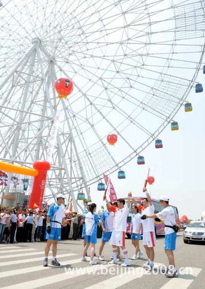 Photo: Two torchbearers relay the Olympic flame under a Ferris wheel