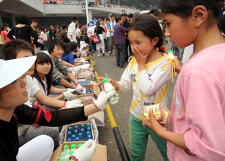 A volunteer gives a bottle of yogurt to a child at the Jiuzhou Stadium in Mianyang City, southwest China's Sichuan Province, May 17, 2008.