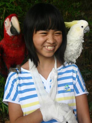 Guo Ling, an injured girl from the quake-ravaged Mianyang City of Sichuan Province, poses for a photo with two parrots while visiting a safari park in southwest China's Chongqing Municipality, May 31, 2008. 