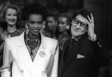 Designer Yves Saint Laurent waves to the audience beside an unidentified model after his Spring-Summer high fashion show in Paris in this January 25, 1989 file photo.