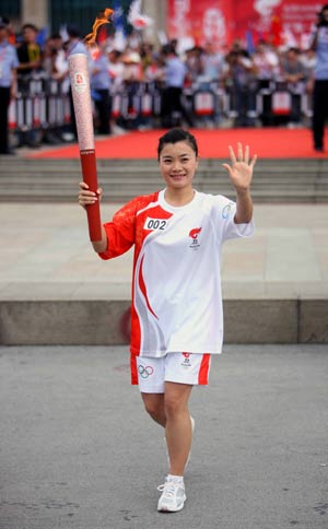 Torchbearer and Olympic gold medal winner Mo Huilan waves to people while running during the 2008 Beijing Olympic Games torch relay in Nanning, southwest China's Guangxi Zhuang Autonomous Region, June 7, 2008. 
