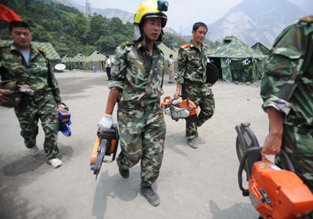 Soldiers carry cutting machines as they set off to the spot where remains of the missing Chinese helicopter were found at Yingxiu Township, Wenchuan County in Southwest China's Sichuan Province on June 10, 2008.
