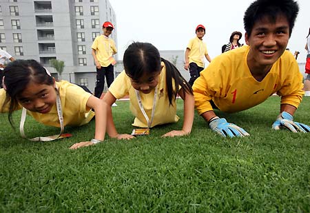 Two deaf girls do pushups with a Chinese soccer team member in Beijing, June 19, 2008. As members of the 56 ambassadors of China's 56 ethnic groups, the two girls will enjoy the host city in a five-day 'Olympic Tour' event until June 23. 