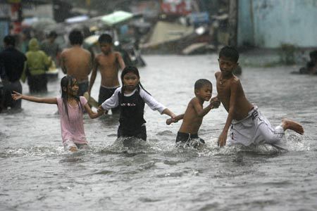 Children wade through knee-deep floodwaters after a Typhoon Fengshen pelted metro Manila with torrential rain and high winds June 22, 2008. [Photo: Xinhua/Reuters]