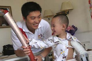 Three-year-old Lang Zheng (R), an earthquake survivor who became an overnight celebrity for a picture of him on a stretcher raising his hand in salute to a quake-relief PLA soldier, holds the Beijing 2008 Olympic torch at a ward in Xi'an, capital of Shaanxi Province, June 23, 2008. Torchbearer Wang Zhen (L) visited Lang Monday. [Xinhua]