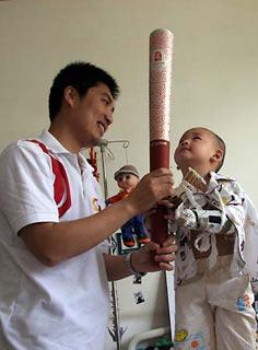 Three-year-old Lang Zheng (R), an earthquake survivor who became an overnight celebrity for a picture of him on a stretcher raising his hand in salute to a quake-relief PLA soldier, holds the Beijing 2008 Olympic torch at a ward in Xi'an, capital of Shaanxi Province, June 23, 2008. Torchbearer Wang Zhen (L) visited Lang Monday. [Xinhua]