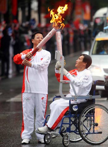 Handicapped torchbearer A Huaimin of the Mongolian ethnic group lights the torch for the next torchbearer Niu Xiaolin during the 2008 Beijing Olympic Games torch relay in Xining, northwest China's Qinghai Province, on June 24, 2008.