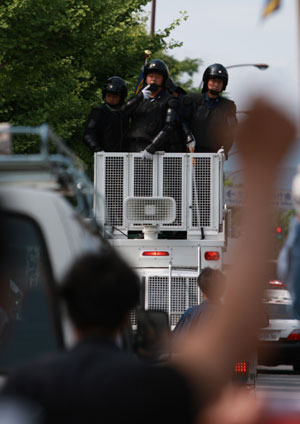 Riot police officers stand guard as anti-G8 protesters wave hands during a rally in Kyoto, western Japan, on June 26, 2008, prior to the two-day G8 Foreign Ministers' Meeting to be held in the city from June 26 to 27.(