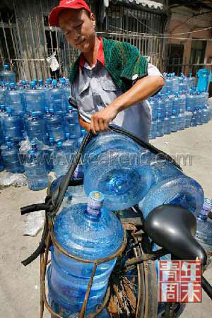 A worker loads bottled mineral water on the rack of his bicycle, ready for delivery. [File Photo: Youth Weekend]