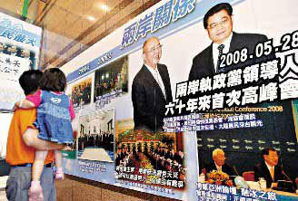 A man, carrying his kid in arms, watches the photo of Hu Jintao meeting with KMT chairman Wu Poh-hsiung in May at the KMT headquarters building in Taipei. [Photo: United Evening News]