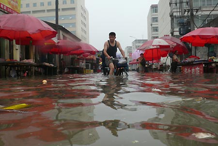 A man rides bike on the flooded Weiming Road in Cangzhou City, north China's Hebei Province, July 5, 2008. Heavy rainfall hit Cangzhou on Saturday. (Xinhua/Fu Xinchun