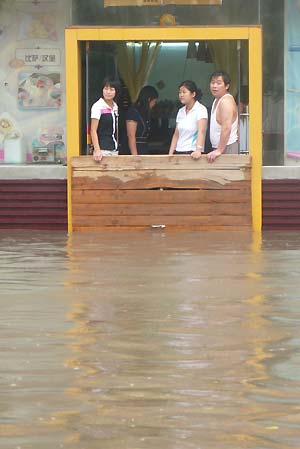 People use a board to block water at the door of a shop on the flooded Weiming Road in Cangzhou City, north China's Hebei Province, July 5, 2008. Heavy rainfall hit Cangzhou on Saturday. (Xinhua/Fu Xinchun)