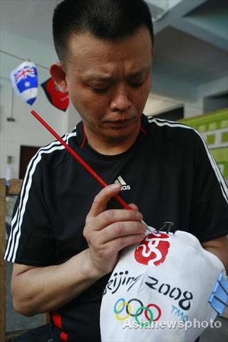 Liu Shihu, a Sichuan opera performer, paints the finishing touches to a mask with the Beijing 2008 Olympic emblem in Suining, Sichuan July 7, 2008. Face-changing, or 'bianlian' in Chinese is a stunt where performers change masks in the blink of an eye in Sichuan opera. [Asianewsphoto]