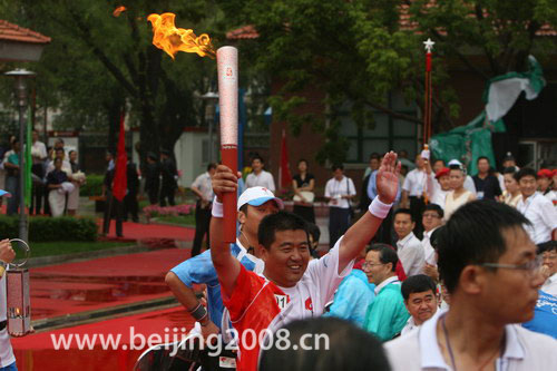 The first torchbearer Hu Zhiqiang waves to locals while running with the Olympic torch in Daqing, Heilongjiang province, on July 12, 2008.