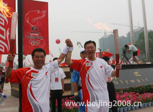 Torchbearers Sun Hongzhi (R) and Wang Gangyi hold their hands together after passing the flame during the Torch Relay in Songyuan, Jilin province, on July 15.