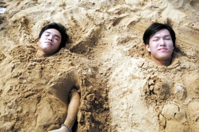 Two citizens in Shanghai municipality bury themselves in sand at City Beach in Jinshan District to cool down on the scorching summer heat on Sunday. An estimated 10,000 people went swimming at the beach each day last weekend. [Photo: Shanghai Morning Post]