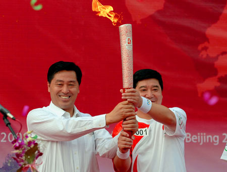 Torchbearer Wang Yifu (R), head coach of the Chinese national shooting team and the country's most experienced Olympian with six successive appearances from 1984 to 2004, receives the torch from Zhang Jiehui, secretary of the Anshan municipal Committee of the Communist Party of China (CPC) during the launching ceremony for the 2008 Beijing Olympic Games torch relay in Anshan, city of northeast China's Liaoning Province, on July 18, 2008. 