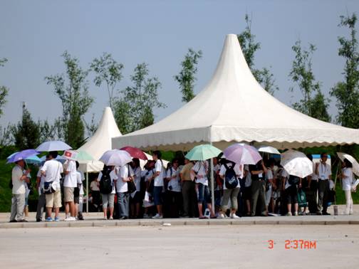 Everyone is standing inside the white tents as all the NOC assistants and athletes are waiting for the buses to come.