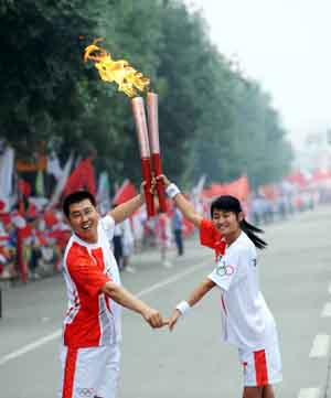 Torchbearer Wang Bo (L) gestures with next torchbearer Liu Fang during the 2008 Beijing Olympic Games torch relay in Tai'an, a city of east China's Shandong Province, on July 22, 2008.