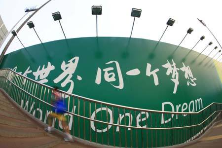 A boy runs past a poster board which reads 'One world, one dream', the slogan of the Beijing Olympic Games July 26, 2008.