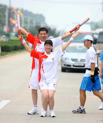 Torchbearer Ren Hanhua (back) poses with the next torchbearer Liu Na during the 2008 Beijing Olympic Games torch relay in Qinhuangdao, a co-host city of Beijing 2008 Olympic Games in north China's Hebei Province, July 30, 2008.