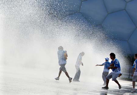 People play at the fountain in front of the National Aquatics Center, nicknamed the "Water Cube", in Beijing, China, July 29, 2008. The sky cleared after a rainfall in some areas of the capital Tuesday.