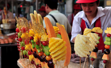 People buy Tanghulu, a Beijing's traditional snack made of sugarcoated haws and other fruit on a stick at a snack booth in a snack street in Beijing, capital of China, July 26, 2008. In the past, the popular Beijing snacks used to be hawked at temple fairs or roadside bazaars. Along with the change of times, traditional Beijing snack bars have emerged in streets and lanes of the city. There are also some snack streets with business of traditional Beijing snacks and other flavor snacks from around China that favor lots of local residents and tourists. 