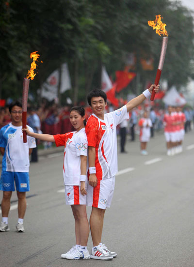 Torchbearer Li Dejia (R) displays the torch with the next torchbearer Li Yipeng during the 2008 Beijing Olympic Games torch relay in north China's Olympics co-host city Tianjin, August 1, 2008. [Xinhua]