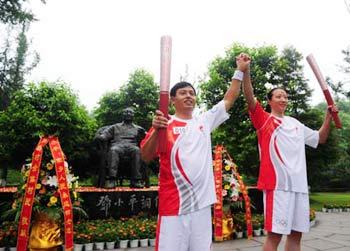 Torchbearer Chen Jing (R) displays the torch with the next torchbearer Li Liangguo in front of the bronze statue of China's late leader Deng Xiaoping during the Beijing 2008 Olympic Games torch relay in Guang'an City, southwest China's Sichuan Province, August 3, 2008. [Xinhua]